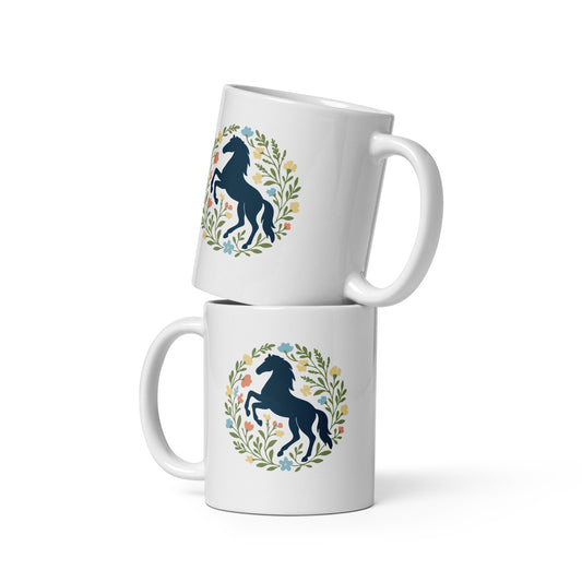 Dunkelblaues, steigendes Pferd umrahmt von einem floralen Kranz in sanften Grün- und Pastelltönen auf weißer Keramik Tasse.