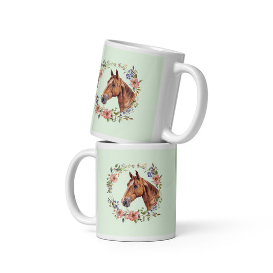 Weiße Keramiktasse mit grünem Hintergrund und Illustration eines Pferdekopfes im Blumenkranz.