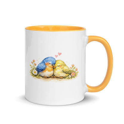 Weiße Keramiktasse mit gelbem Henkel und Innenrand sowie Illustration von zwei kuschelnden Vögeln mit kleinen Herzchen.